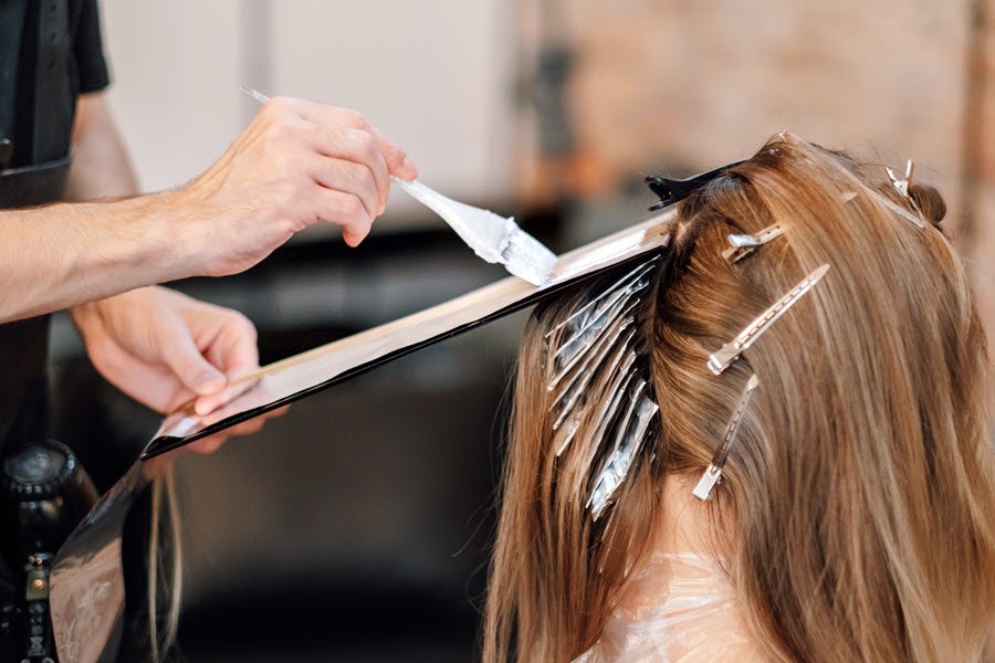 Stylist applying lightener to sectioned hair with foil during a highlight or balayage service.