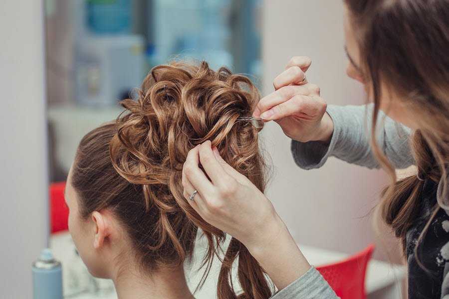 Stylist creating an intricate updo with curls and pins for a formal event hairstyle.
