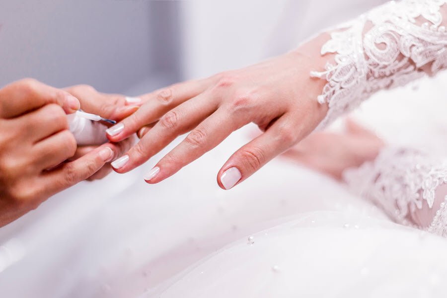 Nail technician applying polish to a bride’s fingernails during a bridal manicure.