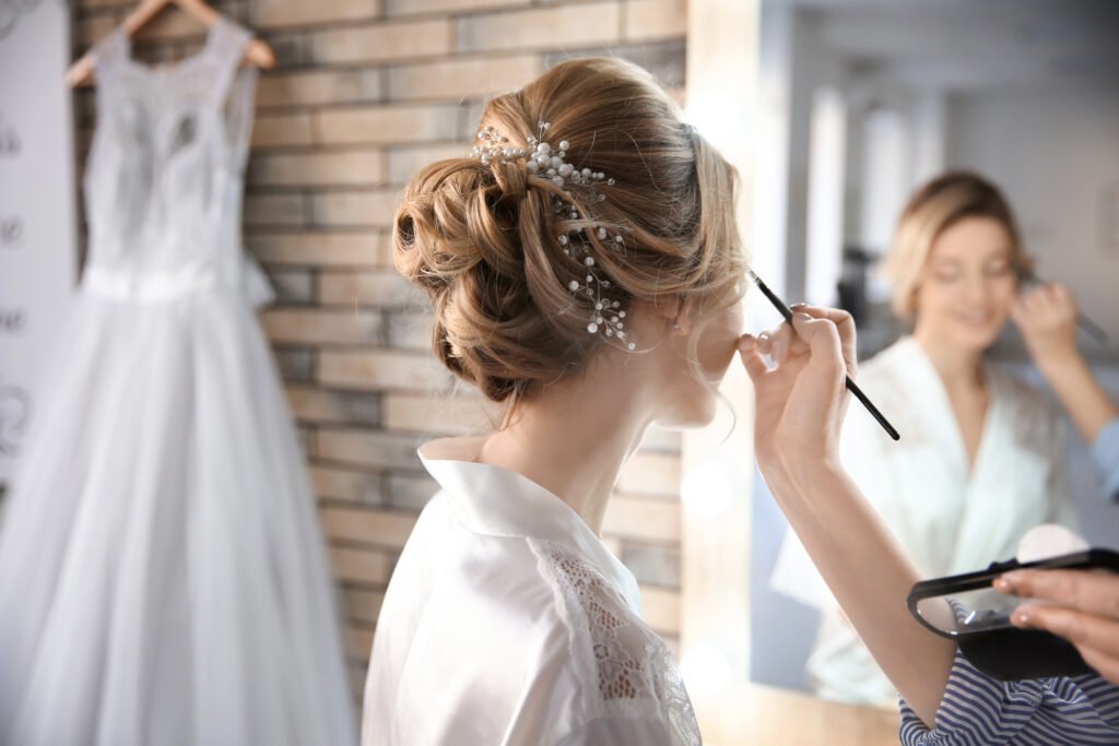 Makeup artist applying eye makeup to a bride wearing a formal updo and bridal robe.