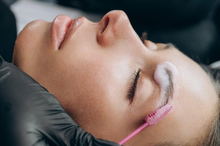 Brow artist brushing eyebrow hairs upward during a brow lamination service.