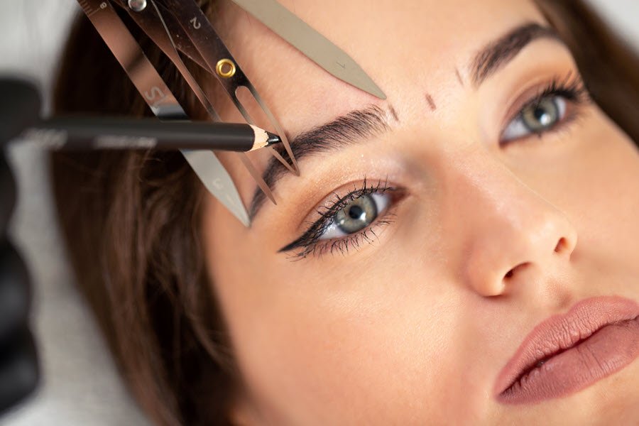Brow artist trimming eyebrow hairs with small scissors during a professional brow shaping service.