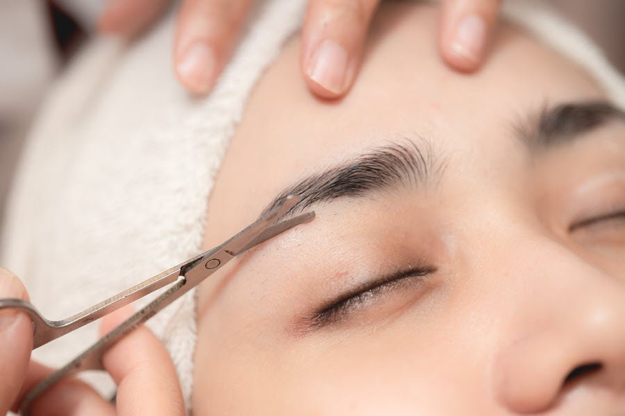 Brow artist mapping and measuring eyebrow shape with a pencil and brow ruler.
