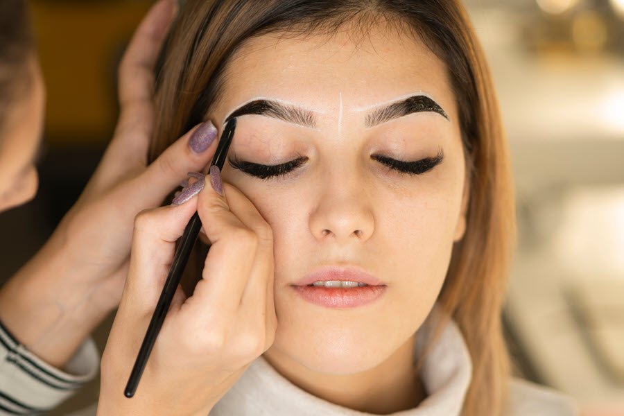 Brow artist applying dark tint to a client’s eyebrows during a professional brow color service.