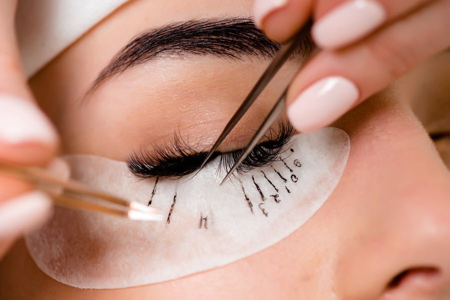Lash technician applying individual eyelash extensions to a client with precision tweezers.