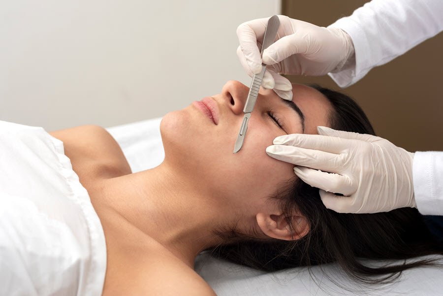 Esthetician performing dermaplaning on a client’s cheek with a sterile facial blade.