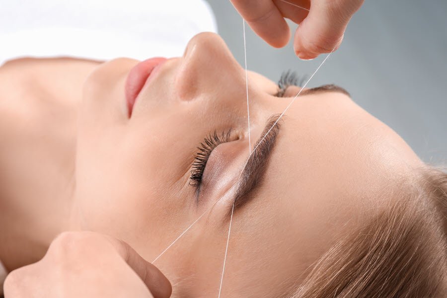 Brow artist threading a client’s eyebrow to remove stray hairs and define the brow shape.