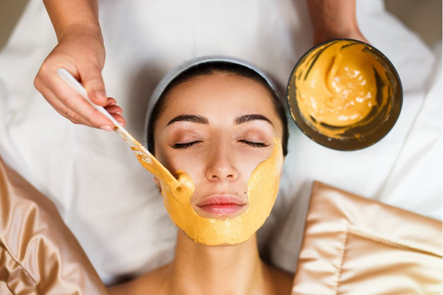 Esthetician applying a treatment mask with a brush during a customized facial enhancement.