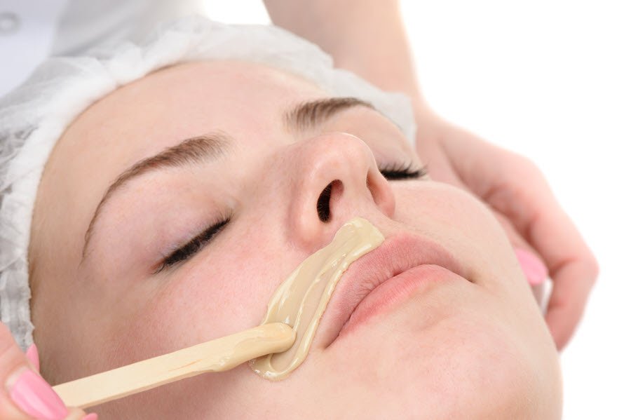 Esthetician applying wax to the upper lip during a professional facial waxing service.