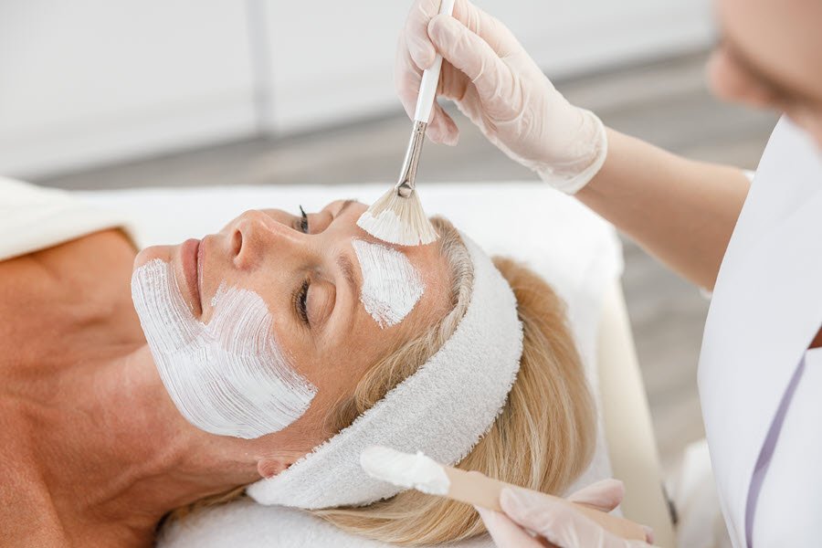 Esthetician applying a facial treatment mask to mature skin during a professional facial.