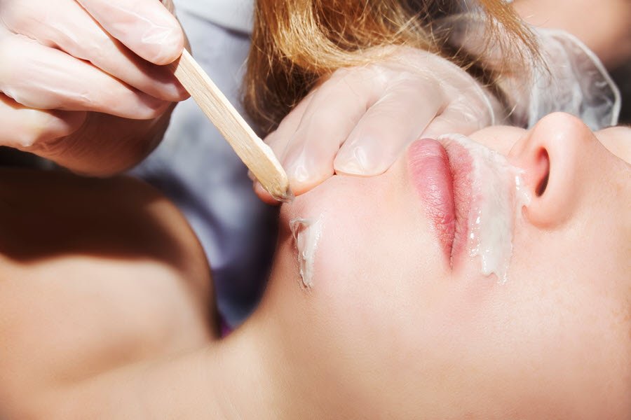 Beauty professional applying wax to a client’s chin and lower facial area during a facial waxing service.