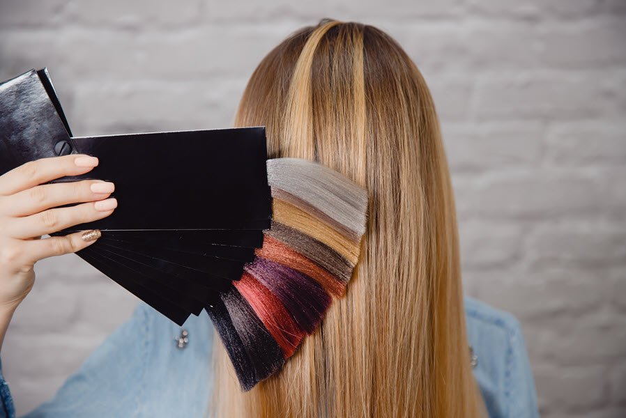 Hair color swatches held beside long highlighted hair during a professional color consultation.