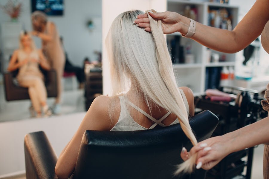 Stylist holding long blonde hair extensions against a client’s hair during an extension consultation.