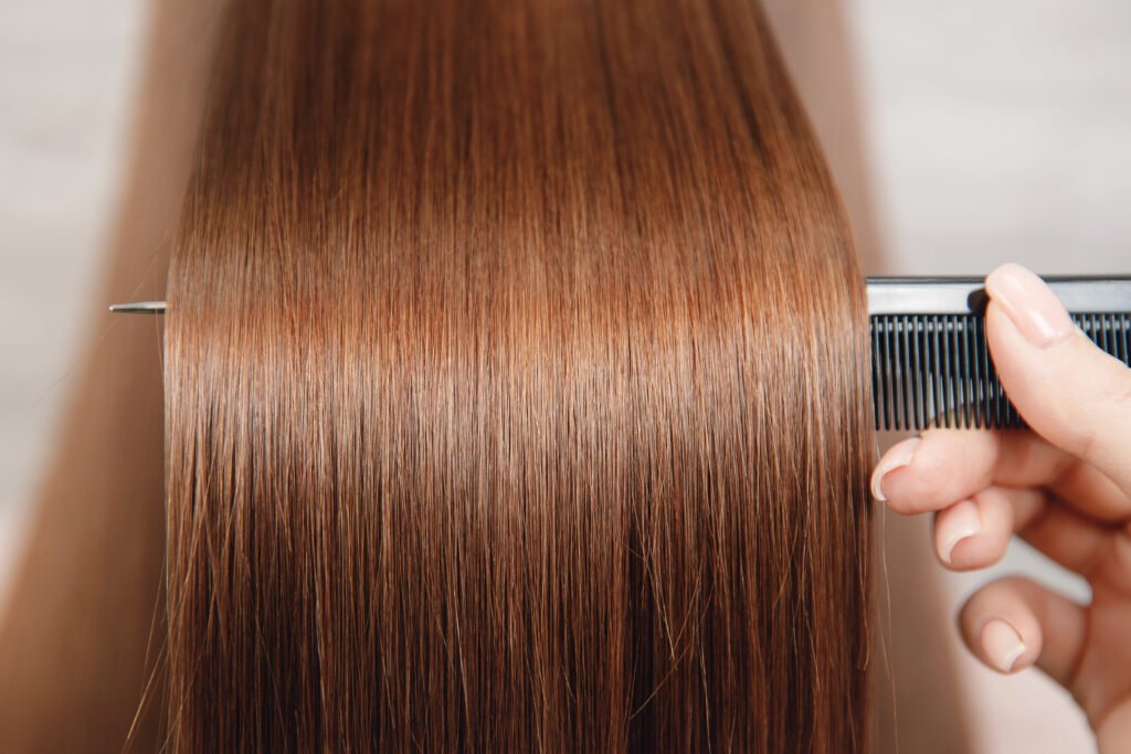 Stylist examining and smoothing long healthy-looking hair during a salon hair treatment service.