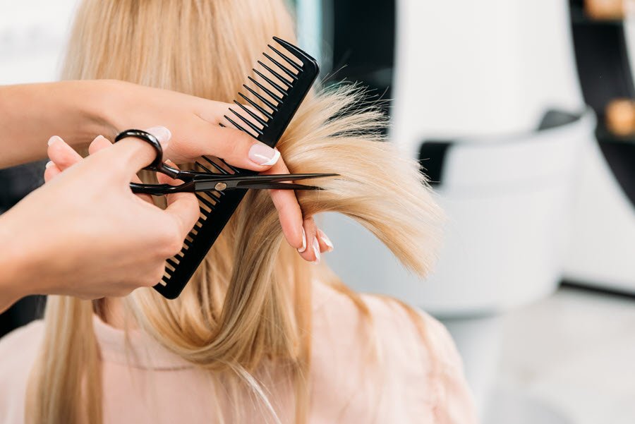 Stylist trimming long blonde hair with scissors and comb during a professional haircut.