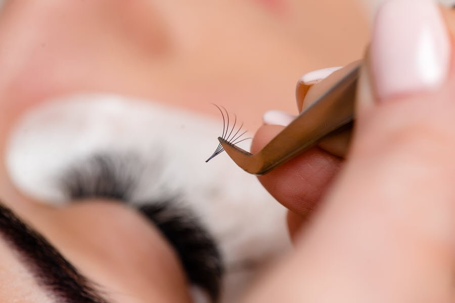Lash technician holding a small fan of eyelash extensions with precision tweezers.