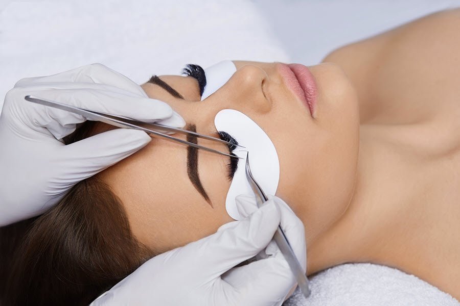 Lash technician applying individual lashes to a client with precision tweezers.