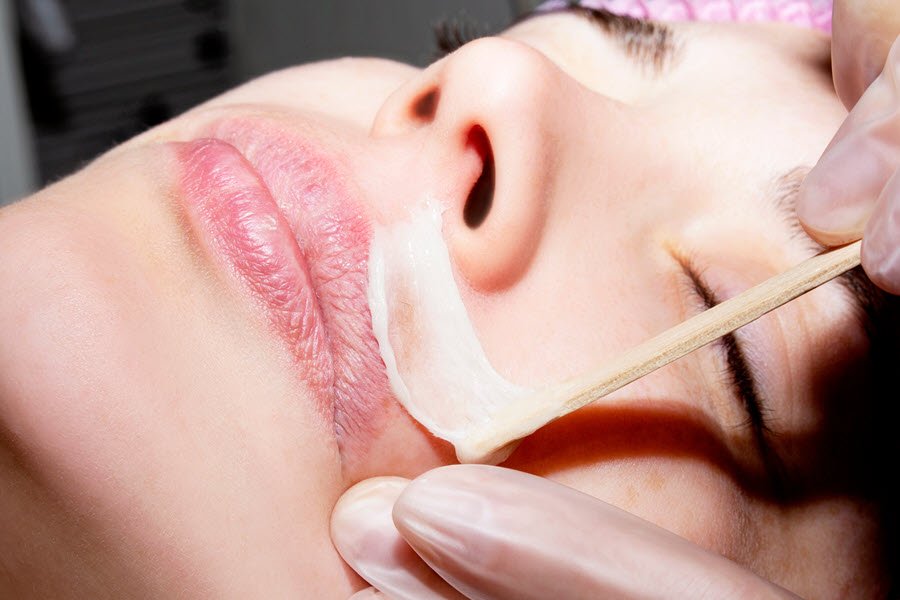 Beauty professional applying facial wax along a client’s upper lip and cheek area.