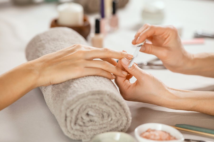 Nail technician filing and shaping a client’s fingernails during a professional manicure.