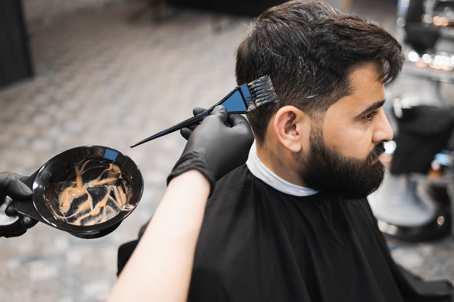 Colorist applying hair color with a brush to a male client’s hair.