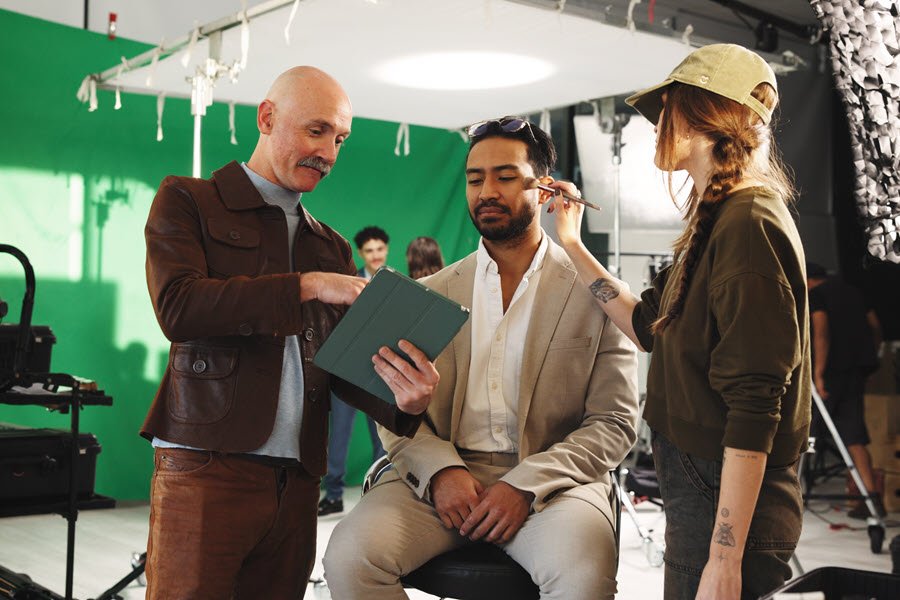 Makeup artist applying face makeup to a male client on a professional photo or video set.