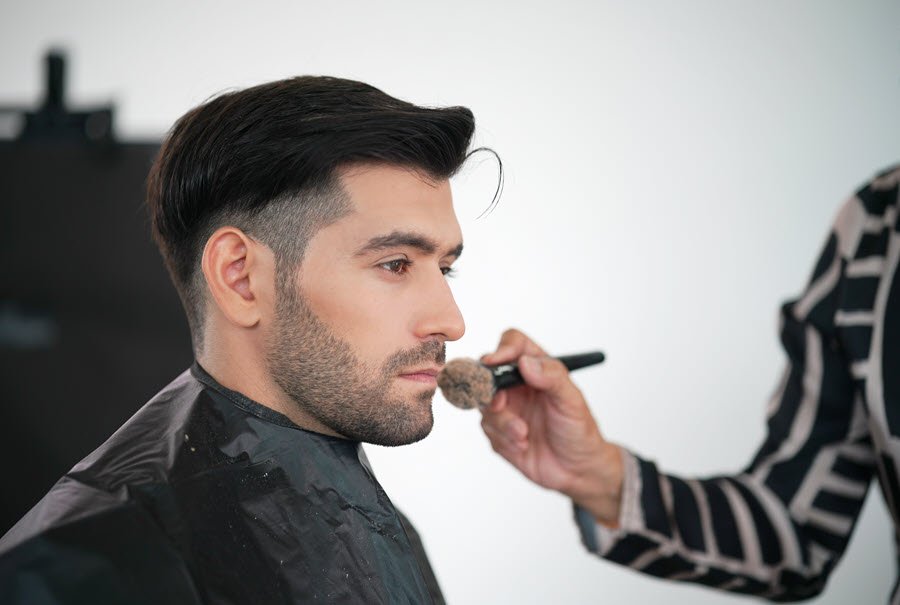Makeup artist applying face powder with a brush during a men’s grooming makeup service.