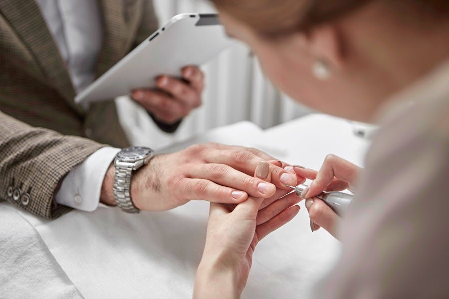 Nail technician shaping a male client’s fingernails during a professional manicure.