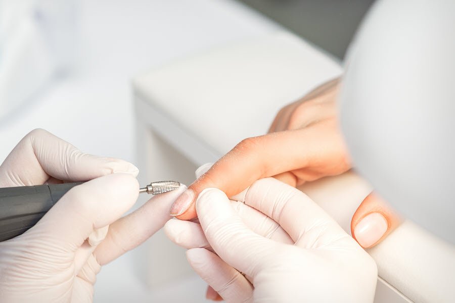 Nail technician using an electric file during professional nail care and product removal.