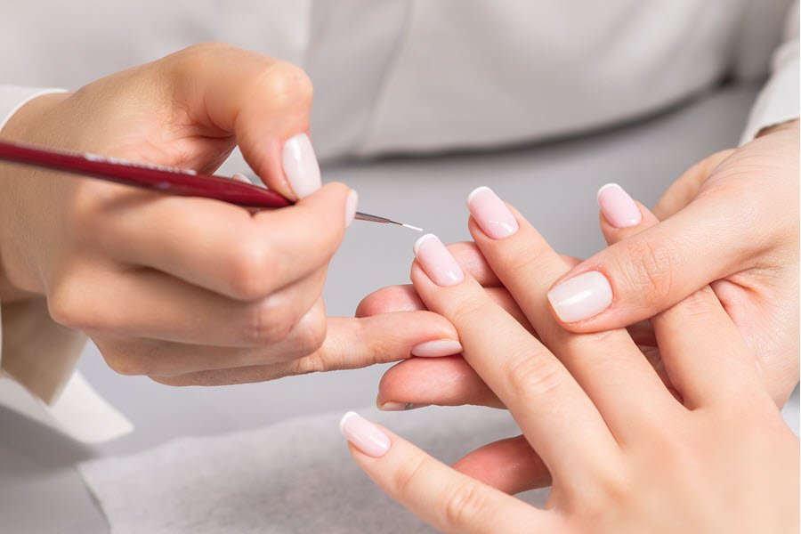 Nail technician applying a white French tip detail to a client’s pale pink manicure.