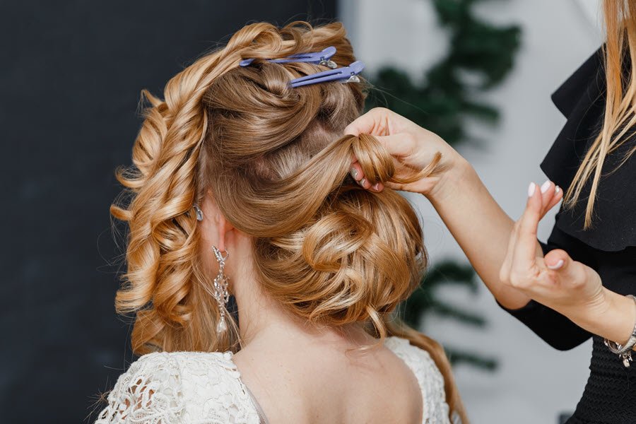 Hairstylist arranging a bride’s curled updo and placing decorative hair accessories.