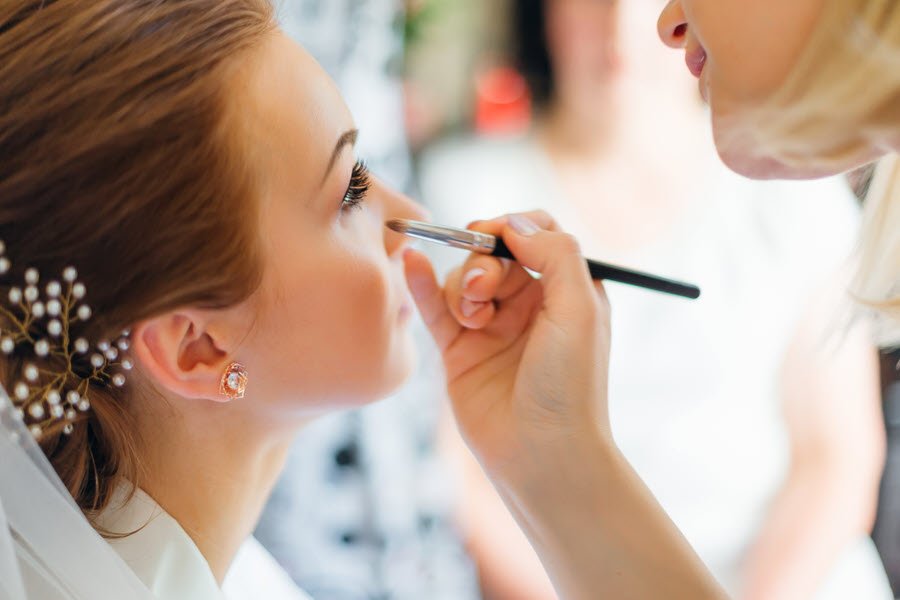 Makeup artist applying face makeup to a bride during a wedding beauty appointment.